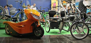 links ein elektrischer Rollstuhltransporter, rechts ein Dreirad mit elektrischem Unterstützungsmotor